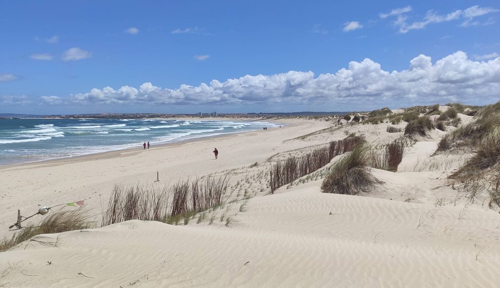 A wide sandy beach backed by dunes, with small waves rolling in under an open sky