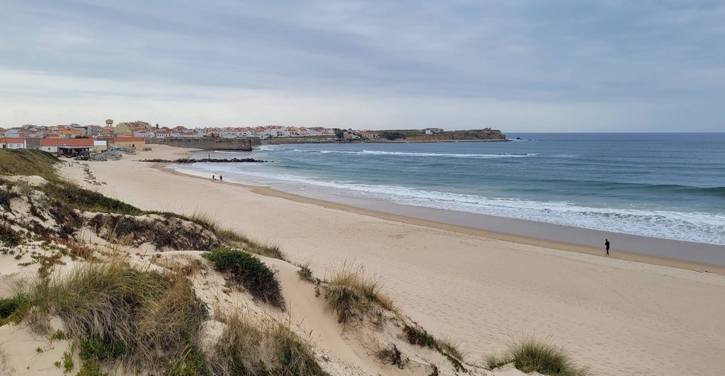 An urban sandy beach next to old stone fortress walls, with small waves and a seafront promenade