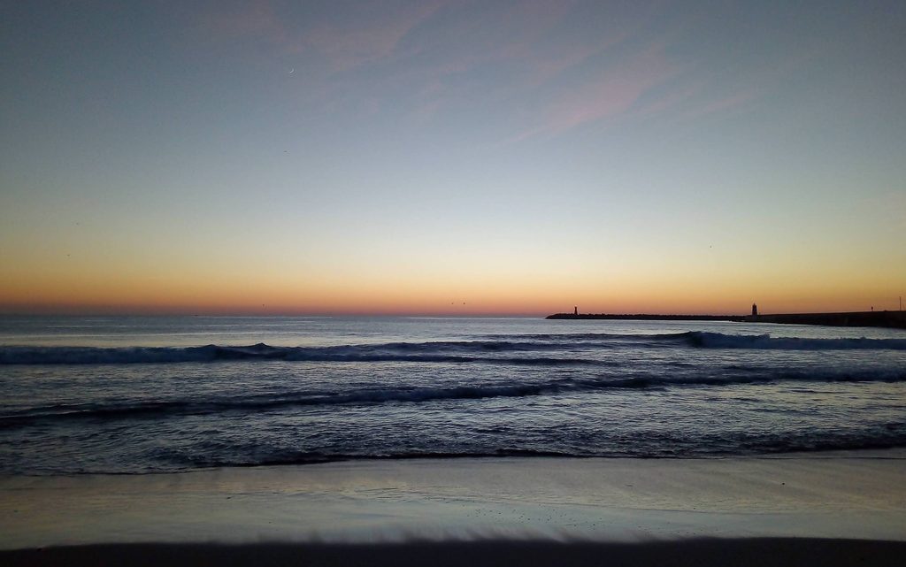 A calm sea at dusk beside a harbour breakwater, with small waves breaking under a fading sky