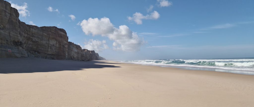 Layered sandstone cliffs beside a wide, empty beach on the Óbidos Coast