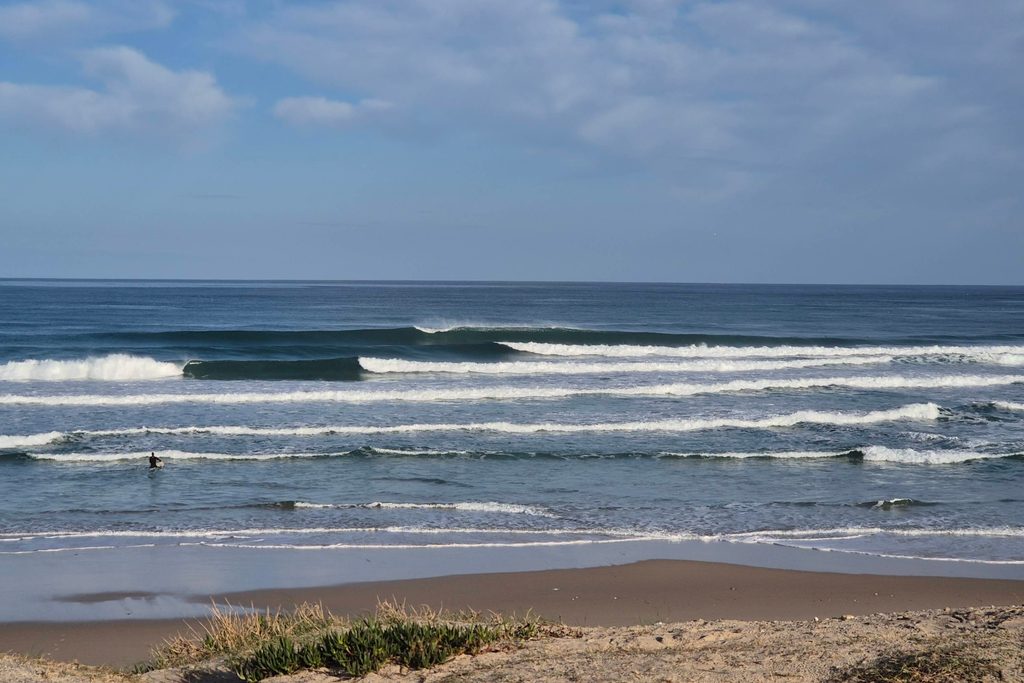 An open, undeveloped sandy beach with dunes and low waves under a wide sky