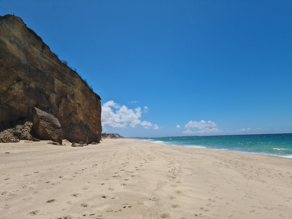 A long sandy beach beneath pale, wind-eroded cliffs with waves rolling in